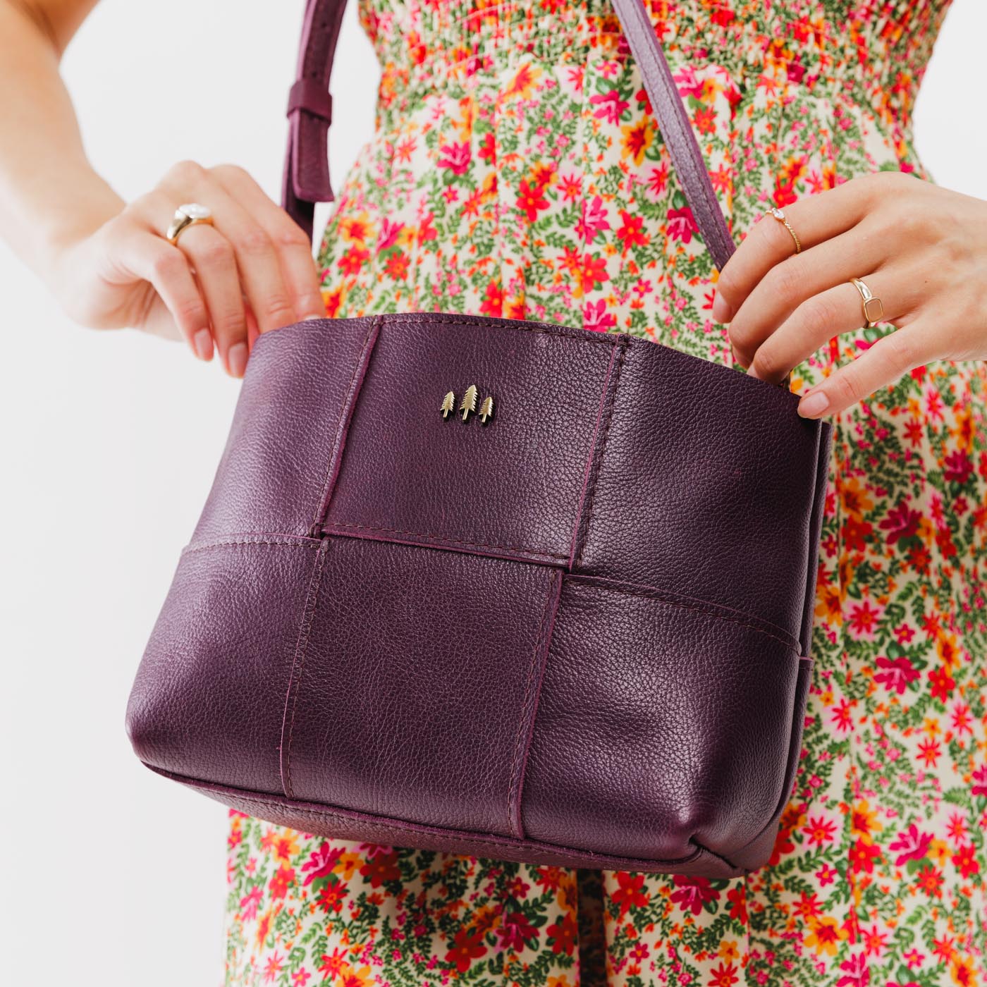 Plum Small | Model carrying structured woven leather bag with three metal tree emblems and crossbody strap