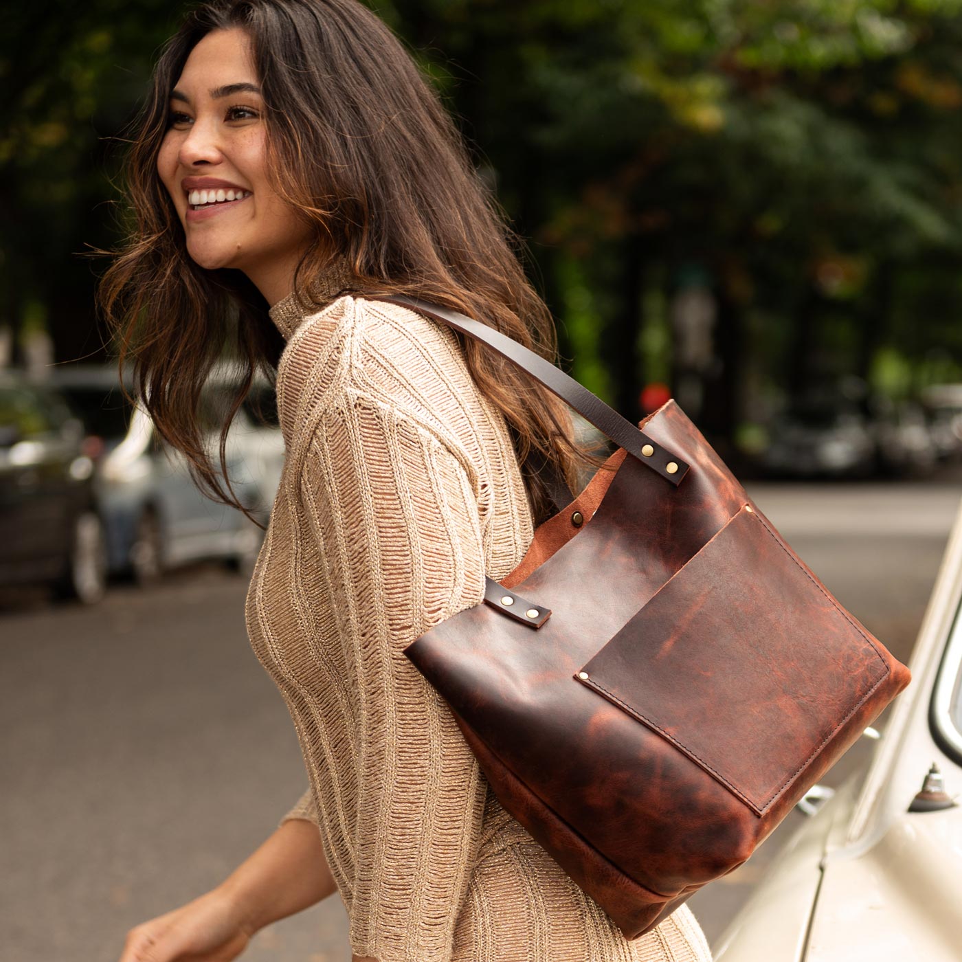 Lava | Model wearing larger leather tote bag with sturdy bridle handles and front pocket outside