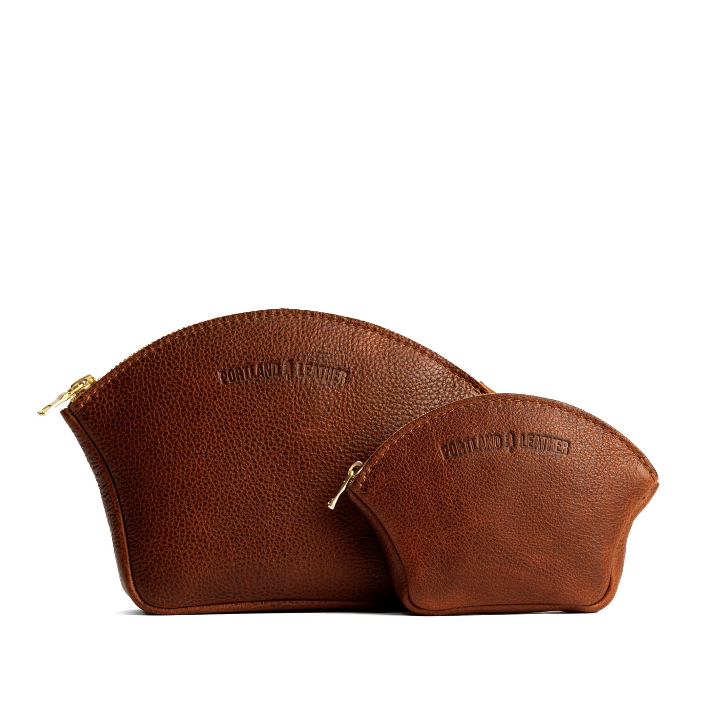 Nutmeg | Comparison shot of small and large seashell shaped leather makeup bags with curved top zipper and flat bottom