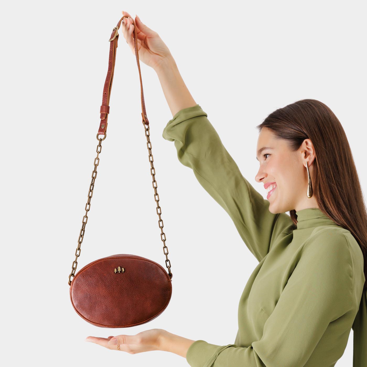 Nutmeg | Model holding oval leather purse with metal crossbody chain strap and adjustable leather shoulder guard