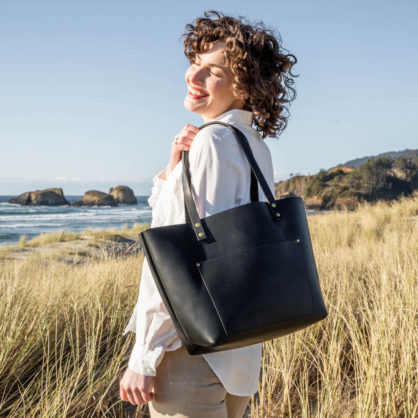 Black  | Model holding large leather tote bag with sturdy bridle handles and front pocket